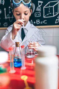 小男孩科学家画肖像从酒瓶中提取液体与粉笔板对面画玩化学液体的严肃孩子图片