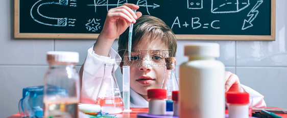 小男孩科学家肖像他们用化学玩具从桌子后面的试验管提取液体图片