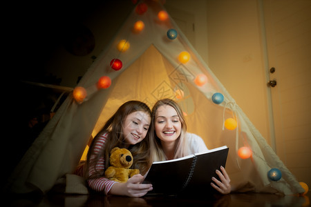 快乐的小女孩和母亲在家中帐篷里一起阅读书图片