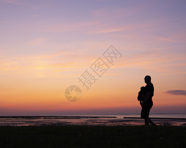 带着孩子在肚中行走的父亲背影面对多彩的日落图片