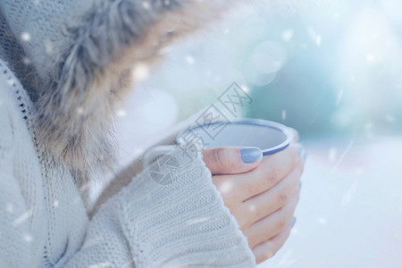 在寒冷的雪地背景下手拿热咖啡或茶的女人穿着暖和的毛皮针织衣服图片