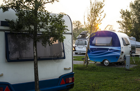 野营的绿色草原上有大篷车和露营者日出早上对露营者进行射线绿草外出旅行的概念和自然界恢复背景图片