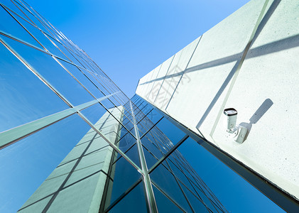 现代办公大楼的照相机部分用玻璃和钢铁面罩着蓝色天空反射镜像图片
