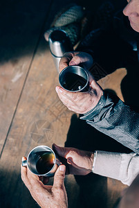 高龄夫妇手握着金属杯子在木制桌上喝咖啡高龄夫妇手握着咖啡杯图片