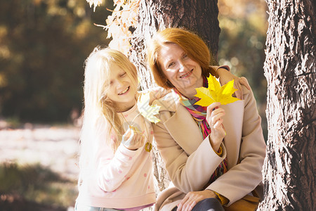 母亲和女儿在公园中手持黄色的红树叶图片