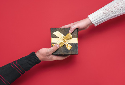 喜庆礼物盒圣诞时间概念男人和女用红色背景的黑礼物盒交换图片