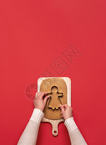 女手切姜饼孩从干面团在一个木制切板和红色背景家里烘烤圣诞节甜点以上观看xmas食品图片