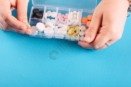 手放在上展示药箱盒和丸蓝色背景图片