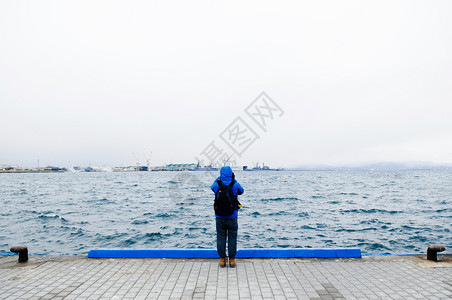 身穿蓝帽衫的人站在海港边缘图片