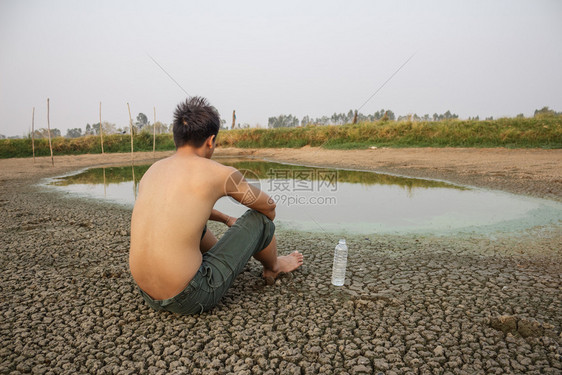 水危机人坐在裂开的地上接近干燥的水图片