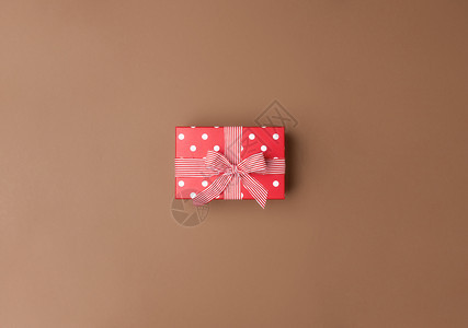 带白点和条纹丝的可爱红色礼物盒棕背景的鞠躬超过圣诞节礼物和弓的视图最小生日礼物图片