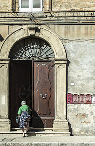 高龄女人进屋典型的意大利式木门房子古老的屋外观阳光圆门拱石头盖房子铁门把手图片