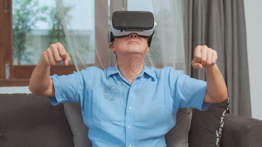 年长的男快乐和虚拟现实玩游戏在家里的客厅躺在沙发上图片