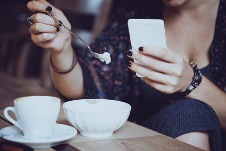 女孩用智能手机坐着喝咖啡和甜点图片