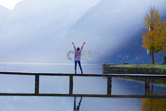 清晨女孩站在山湖上的木桥美丽风景和反光图片