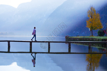 清晨女孩站在山湖上的木桥美丽风景和反光图片