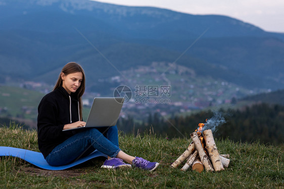 女孩坐在草地上工作营火点燃在边工作图片