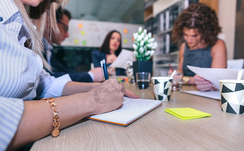 妇女在公司总部办桌旁举行有团队精神的会议在有团队精神的会议上撰写笔记图片