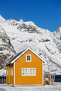 传统的挪威木制屋在峡湾的岸边和远处山上站立图片