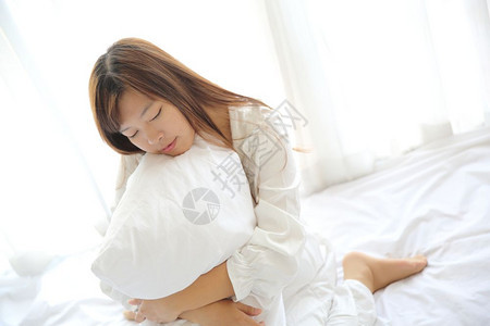 年青的女人醒来时带着枕头睡在白房里图片