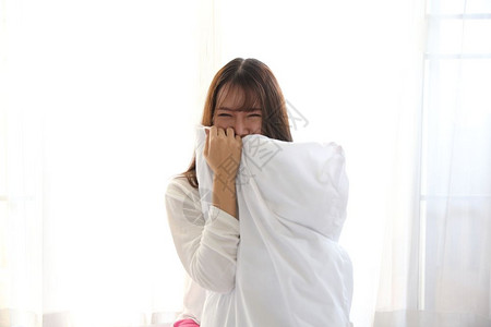 面对窗口年轻亚洲女在白色卧室微笑背景