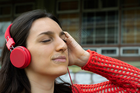 年轻女在户外用红耳机收听音乐的肖像图片