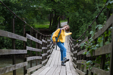 女孩徒步旅行者背包站在悬吊桥上图片