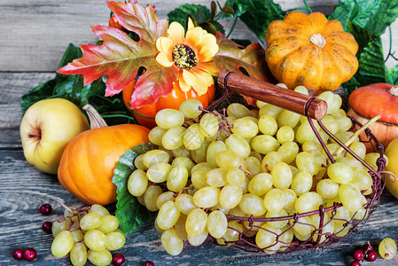 篮子中的绿葡萄和成熟苹果红莓橙色装饰南瓜和木本底有叶子的南瓜图片