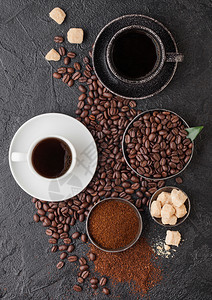 黑白两杯新鲜生有机咖啡配豆子和甘蔗糖块的地面粉末黑底咖啡树叶图片