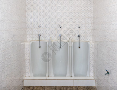 一套三个并排的全长男式便池靠在小卫生间的瓷砖墙上瓷砖浴室或卫生间墙上连续三个全长小便器图片