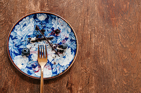已经吃过的蓝莓奶酪蛋糕在美丽的奢华陶瓷盘上留下一些污渍在木桌上有铜叉图片