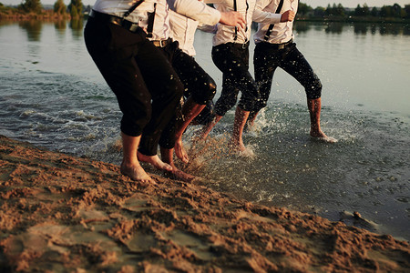 男人和脚在水中穿着服装的男人在水中奔跑他们正在玩乐耍和周围泼水夏天一群快乐的年轻男子在海上浇水滩喷洒水图片