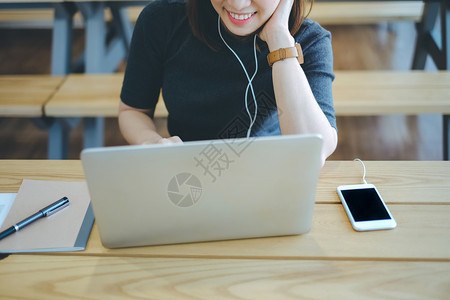 年轻笑的女商人用她的智能手机聆听音乐在办公室或咖啡馆使用笔记本电脑生活方式和商业概念图片