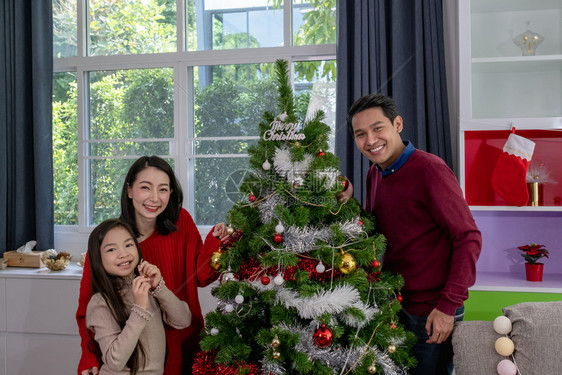 亚足幸福的家庭父亲母女儿帮助准备和赠送或装饰在客厅的圣诞树或装饰图片