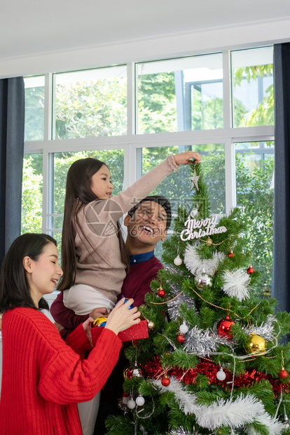 亚足幸福的家庭父亲母女儿帮助准备和赠送或装饰在客厅的圣诞树或装饰图片