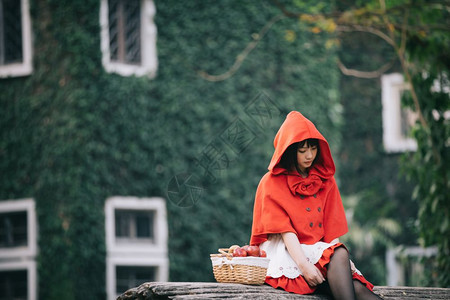 肖像坐在绿树公园背景下身着小红色兜帽装饰的年轻女子身穿绿树公园背景的篮子上图片