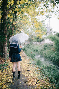 下雨时在自然行走道上带着雨伞行走的亚裔女学生肖像图片