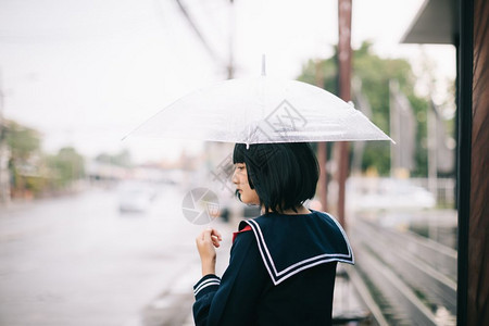 下雨时在自然行走道上带着雨伞行走的亚裔女学生肖像图片