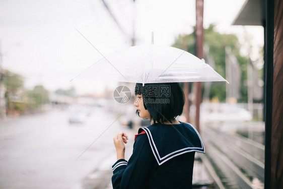 下雨时在自然行走道上带着雨伞行走的亚裔女学生肖像图片