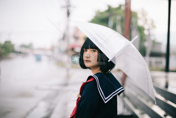 雨天时在乌拉班人行道上带着雨伞走的亚裔女学生肖像图片