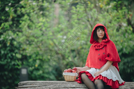 肖像坐在绿树公园背景下身着小红色兜帽装饰的年轻女子身穿绿树公园背景的篮子上图片