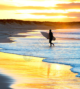 冲浪者在沙滩上行走时的背影日落有冲浪板图片