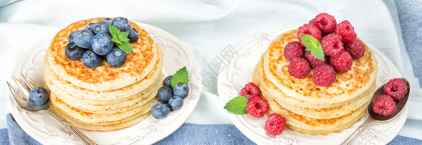 两堆薄煎饼上面装饰着成熟的红莓和蓝以白餐巾纸为背景图片