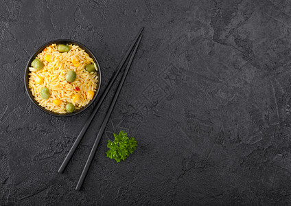 黑碗加煮的有机巴斯马提蔬菜大米黑色的筷子在背景黄的玉米和绿豆子与辣椒片图片