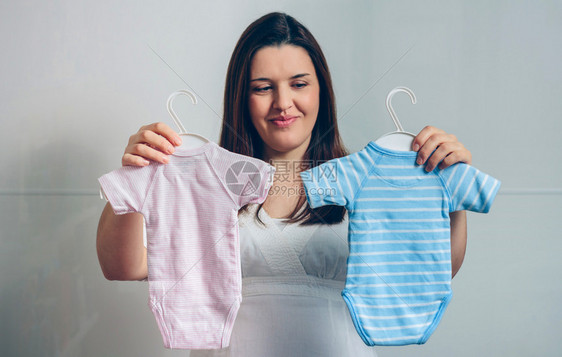 在室内选择婴儿服的孕妇图片