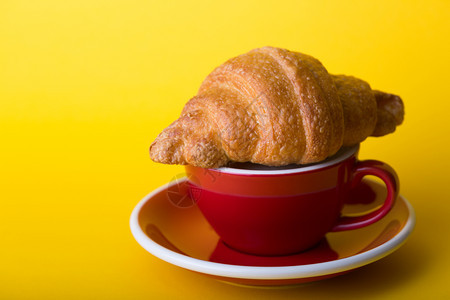 黄底带卡布奇诺和羊角面包的美丽咖啡红杯图片