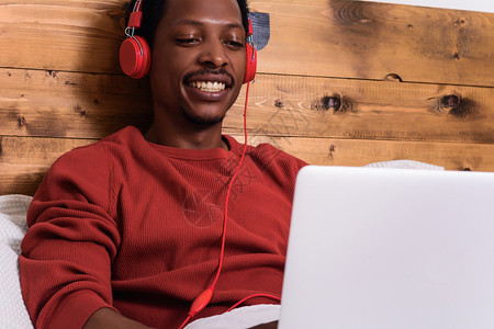 快乐的年轻人用耳机听音乐在床上用笔记本电脑图片