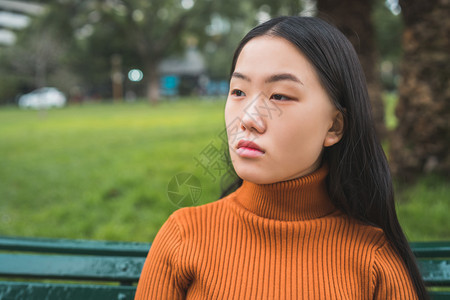 坐在公园户外的长椅上年轻美丽的亚洲女人肖像图片