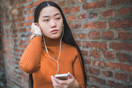 年轻女使用手机与户外耳在街上使用手的肖像图片