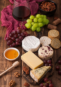 玻璃红葡萄酒在板上挑选各种奶酪和木制桌底的葡萄蓝色stilon红色的李斯特脆奶酪和蜂蜜图片